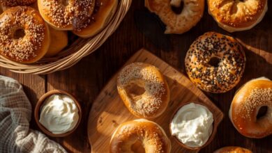 Overhead spread of fresh sesame, everything and plain bagels in a basket and on a wooden board with cream cheese