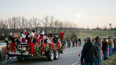 A decorated Christmas parade float rolls along a two-lane Middle Tennessee road as families watch from the shoulder, with bare winter hardwoods, a brick church steeple and a water tower behind (illustrative)