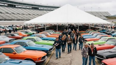Rows of classic muscle cars under an auction tent at a speedway (illustrative)